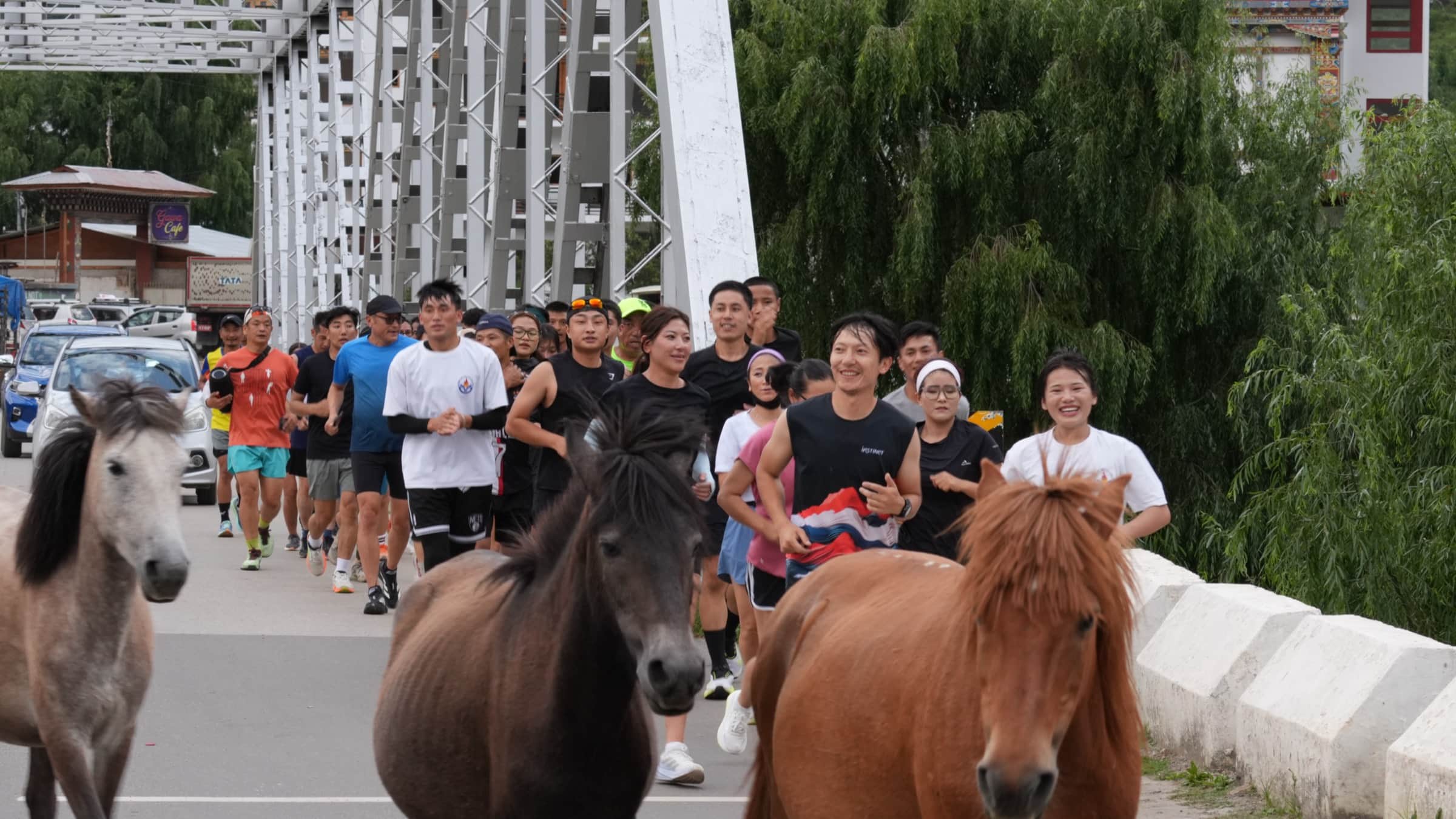 Runners crossing the historic iron bridge alongside Bhutanese horses
